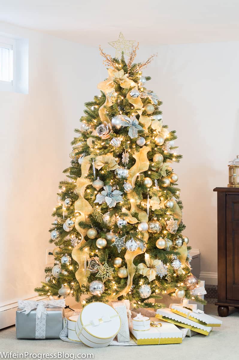 A Christmas tree with clear lights and gold ribbon cascading down, with gold ornaments and flowers