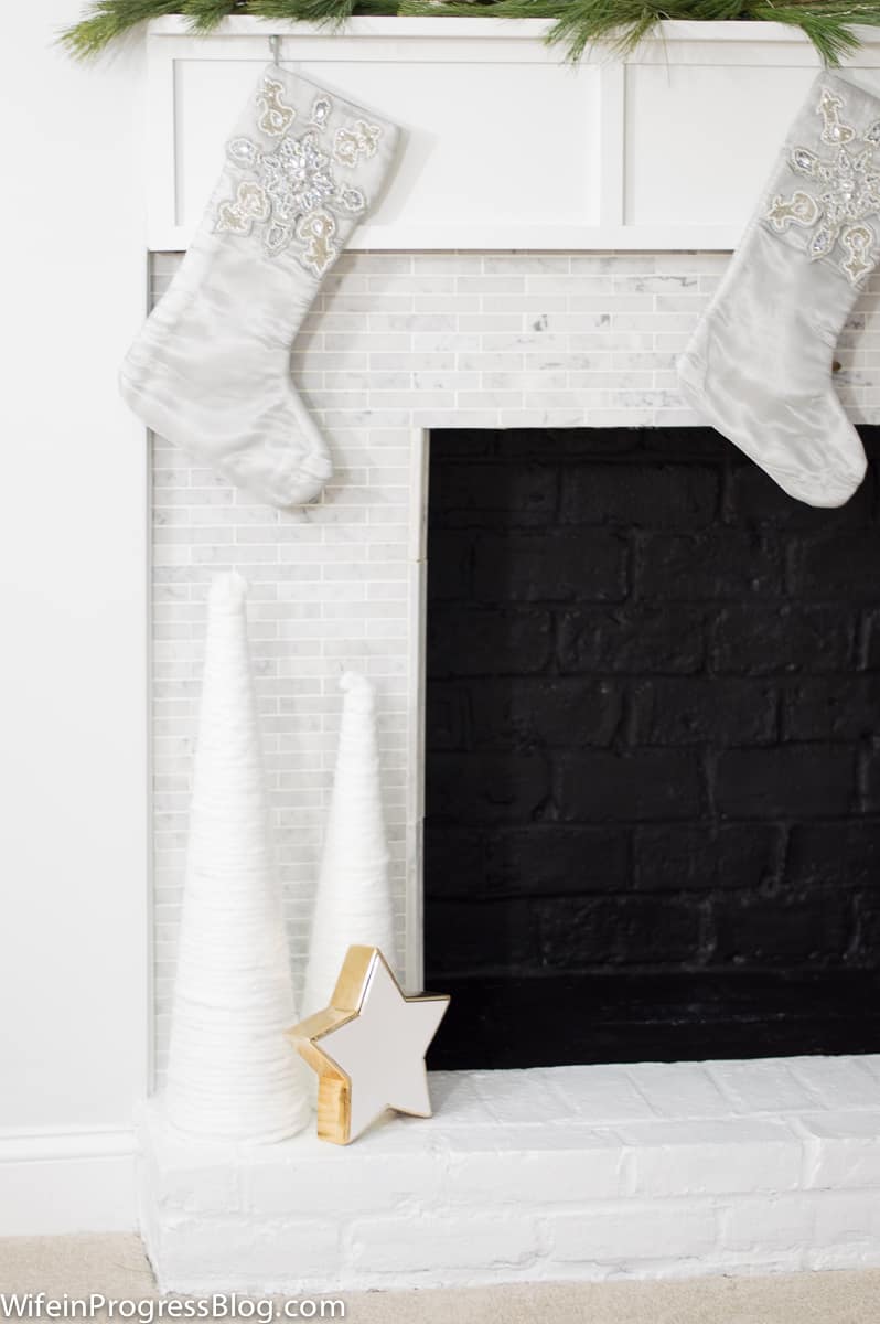 The corner of a fireplace, with grey stockings, tall, white cones resembling trees and a white star with gold trim