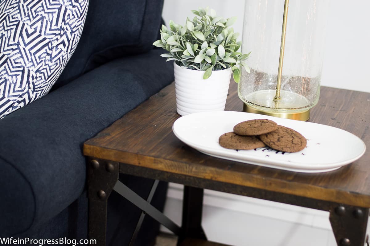 3 chocolate cookies on an oval, white platter near a white plant pot and a lamp with a clear glass base and gold trim