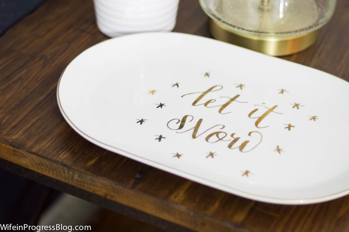 A close-up of an oval, white platter with the words \"let it snow\"