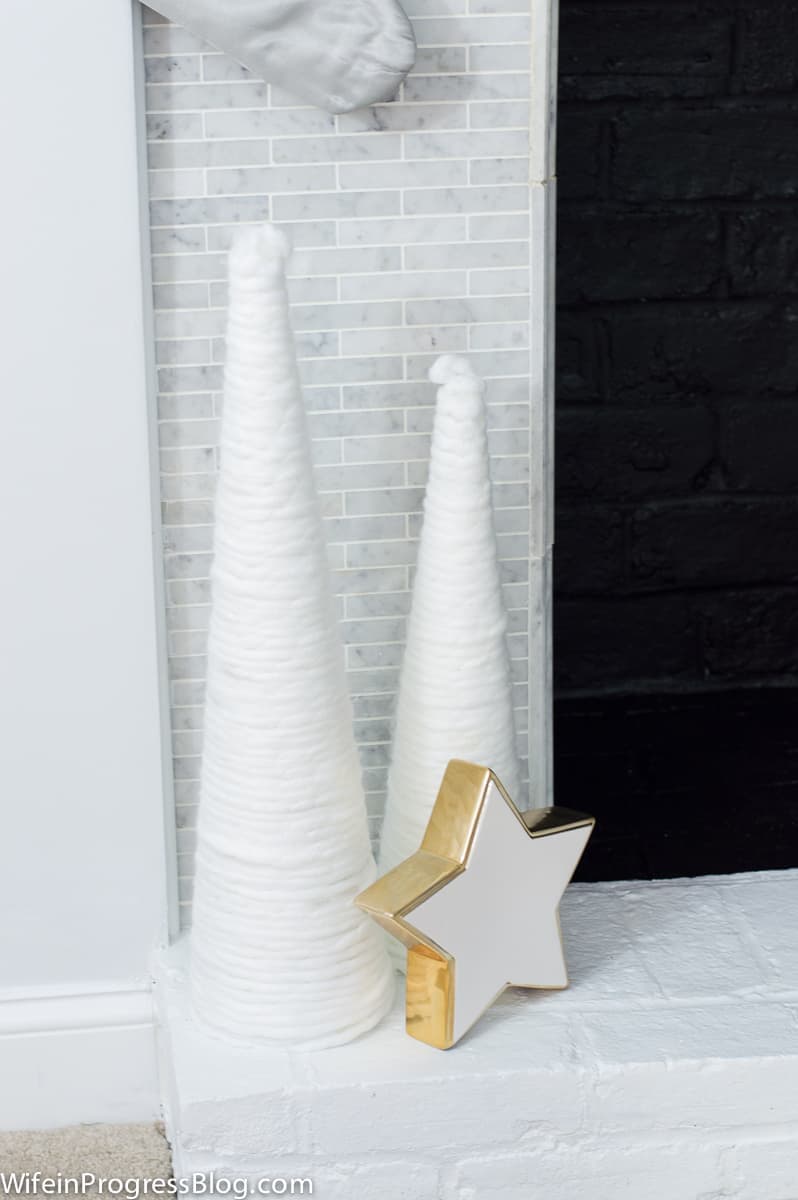 Two tall, white cones resembling snow-covered trees and a white star with gold edges, sitting at the base of a fireplace