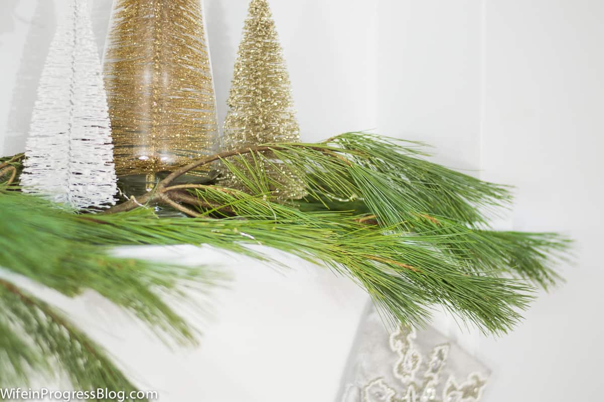 Pine branches and small, gold trees on top of a white fireplace mantel