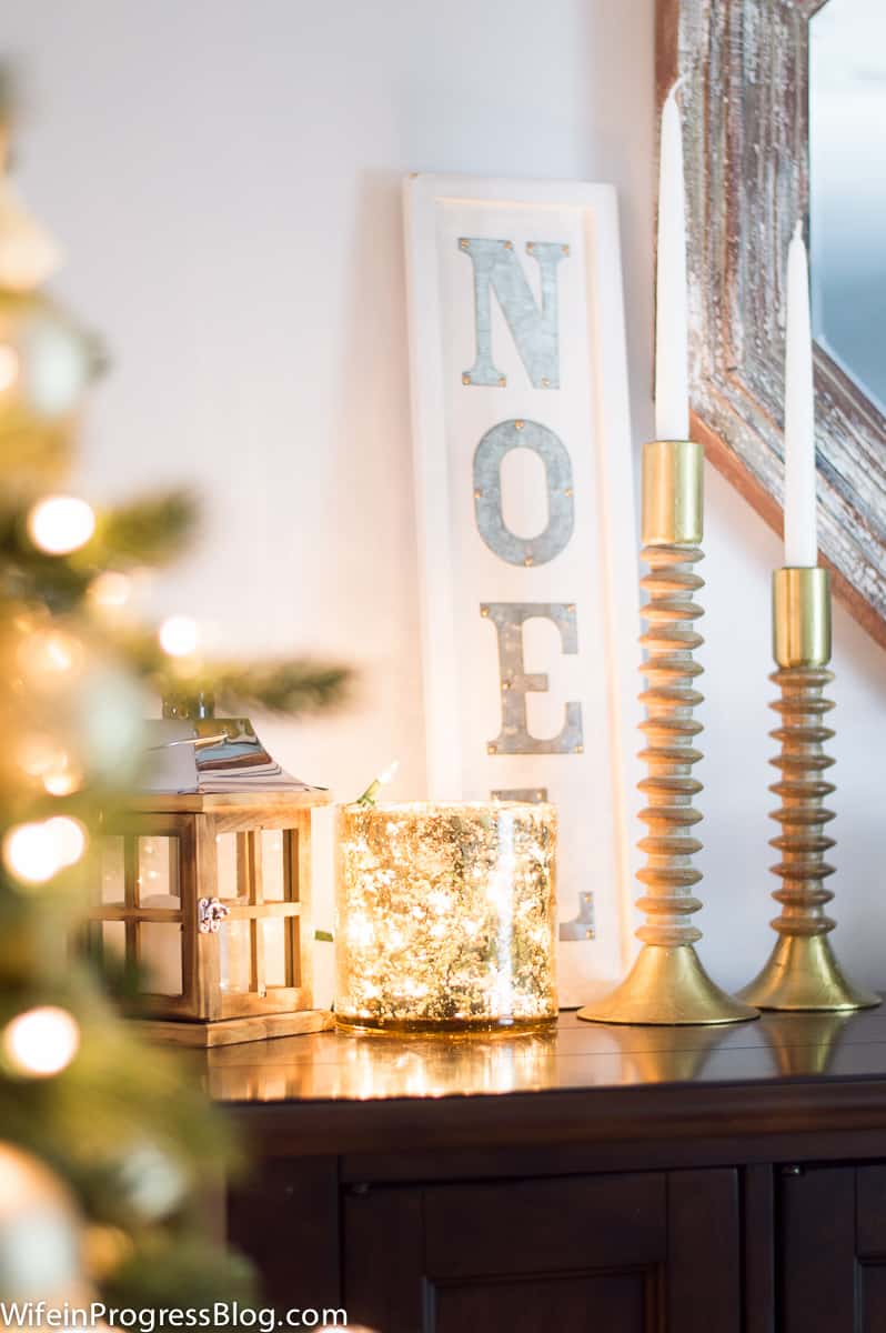 A table near the Christmas tree with a lantern, gold candlesticks, and other holiday decor in gold tones