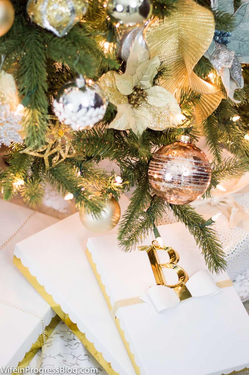 The bottom of a tree with gold flowers and ornaments, and two rectangular gift boxes with gold trim and white ribbon