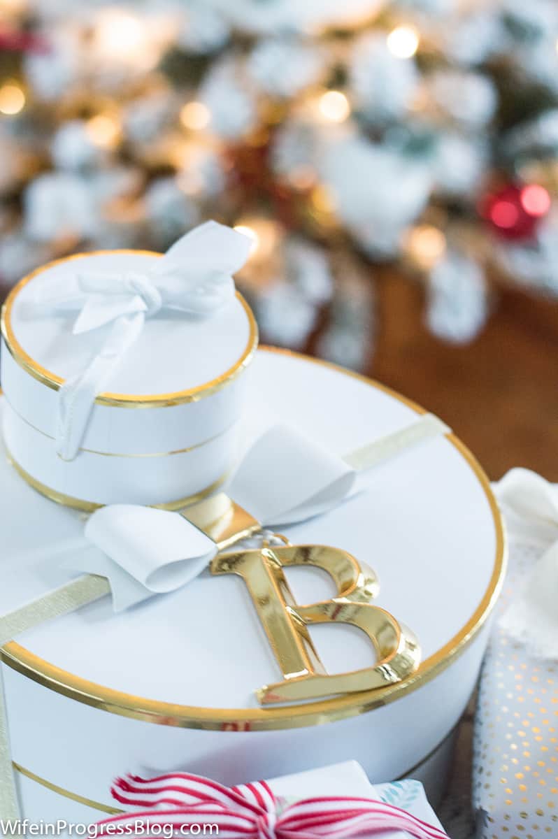 Round, white gift boxes with gold trim and white bow on top, with a gold initial \"B\" attached to the larger box
