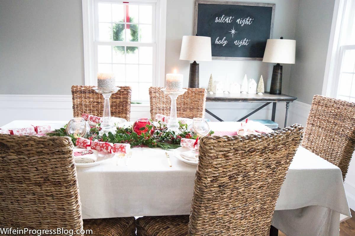A dining table with a white tablecloth, red and white napkins and greenery in the center with red accents