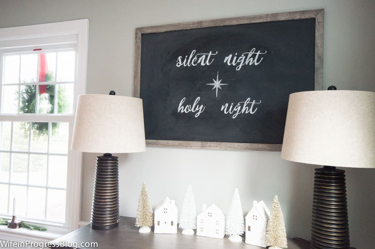 The words \"silent night, holy night\" written in chalk on a large blackboard, above a side table