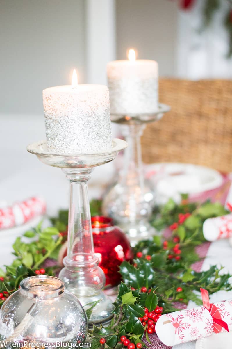 Glittery silver candles rest on tall pedestal candle holders on a holiday-themed tablescape
