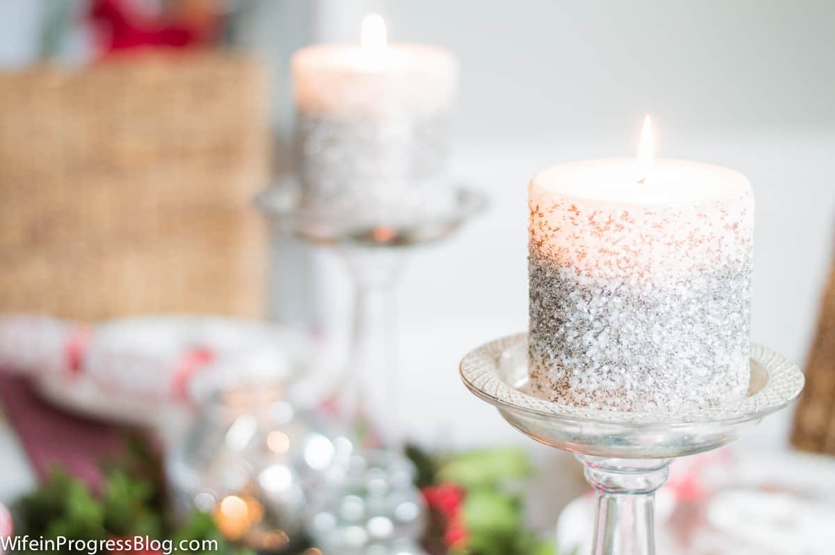 A close-up of the short, wide candles with glittery sides, resting on tall, glass candle holders on a table