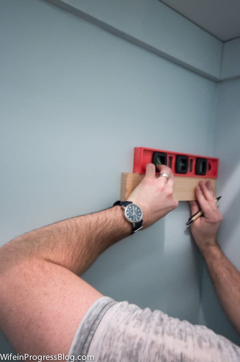 A person holding a level against a thin piece of wood being attached to the wall 