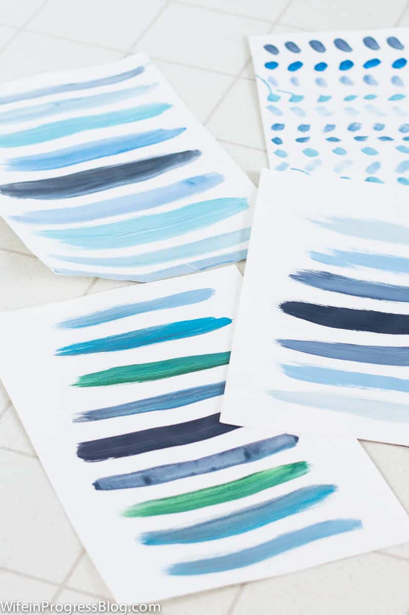 Practicing blue brush strokes on different pieces of paper on a tiled floor