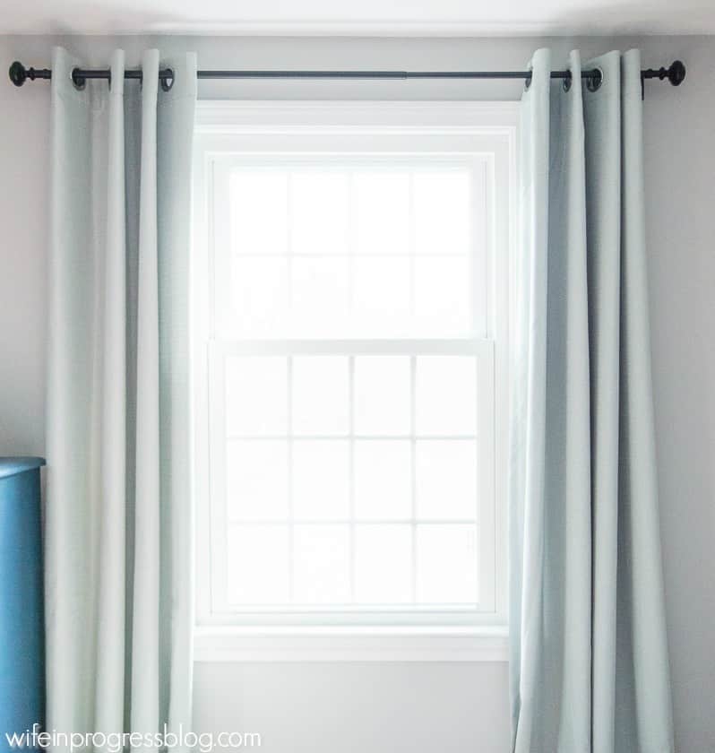 A pair of pale blue/green curtains hung from a black rod of a single window