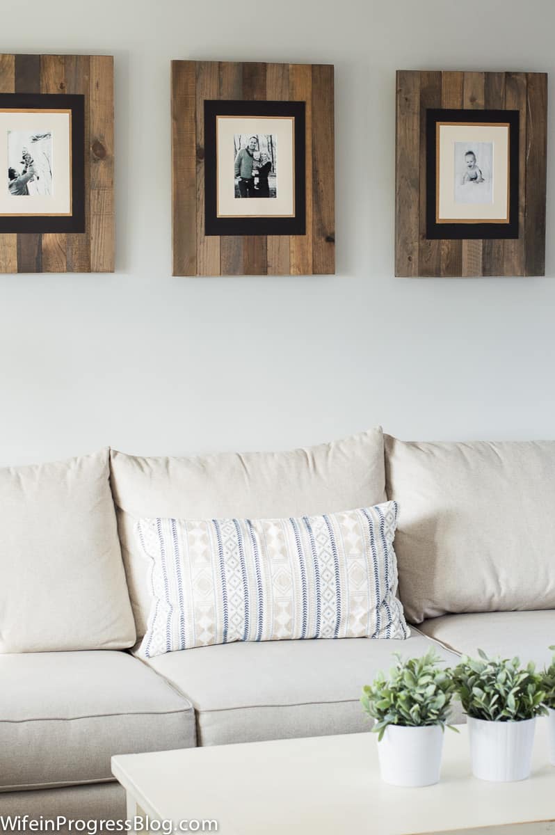 Three wooden frames in natural finish with family portraits above an off-white sofa