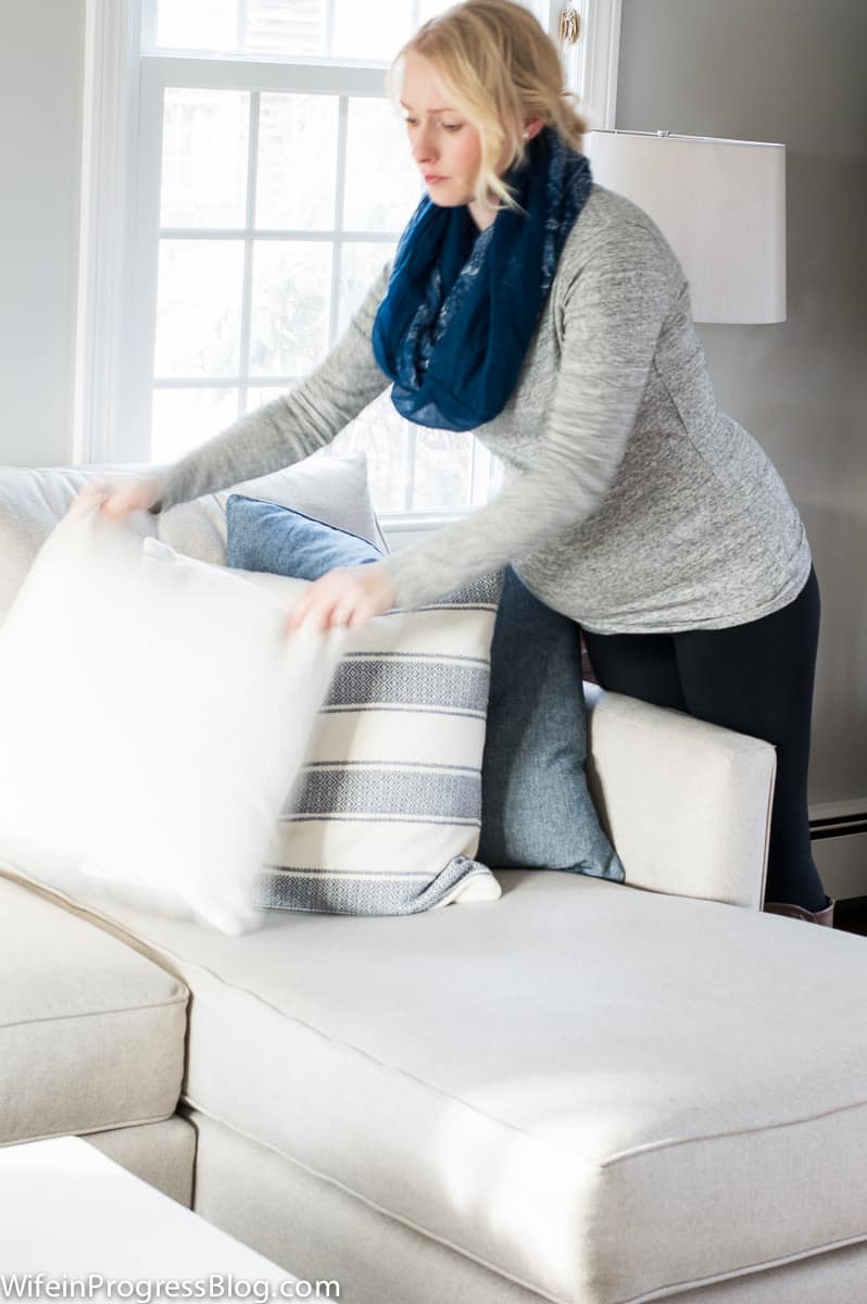 A woman adjusting throw pillows on the sofa in the living room