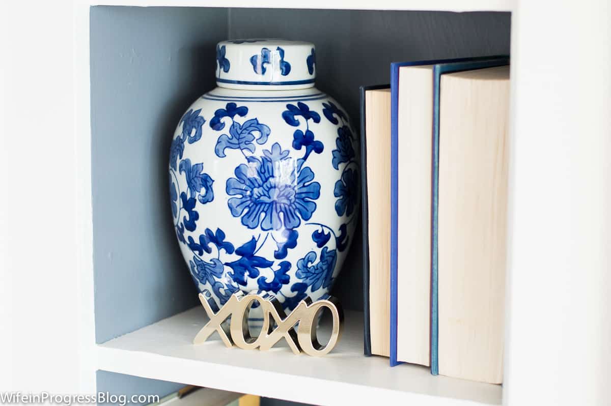A large, blue and white vase on a shelf, near books with the pages facing outwards (instead of spines)