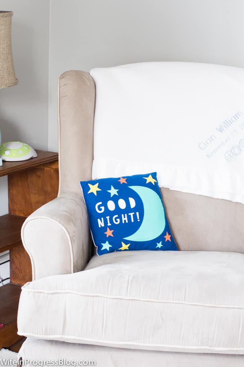 A beige armchair with a personalized, white blanket and a small blue pillow with the words \"Good Night!\"