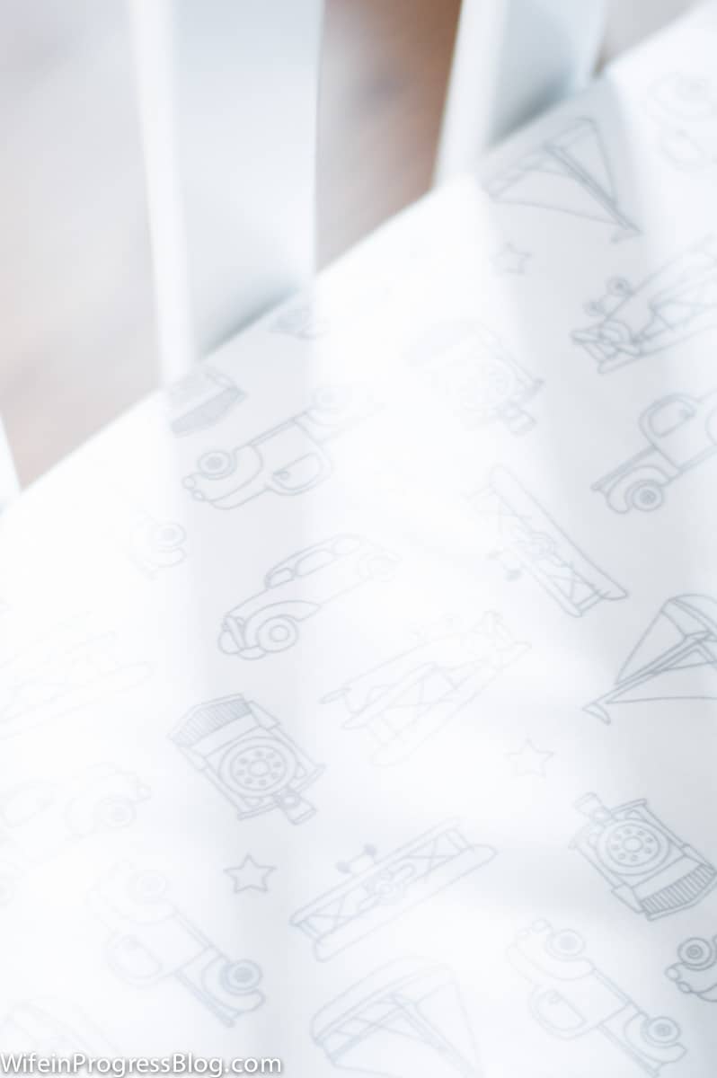 A close-up of white crib sheets with line drawings of boats, cars and sailboats
