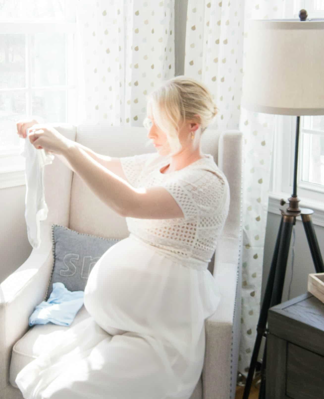 Mother folding onesies in white chair in baby nursery