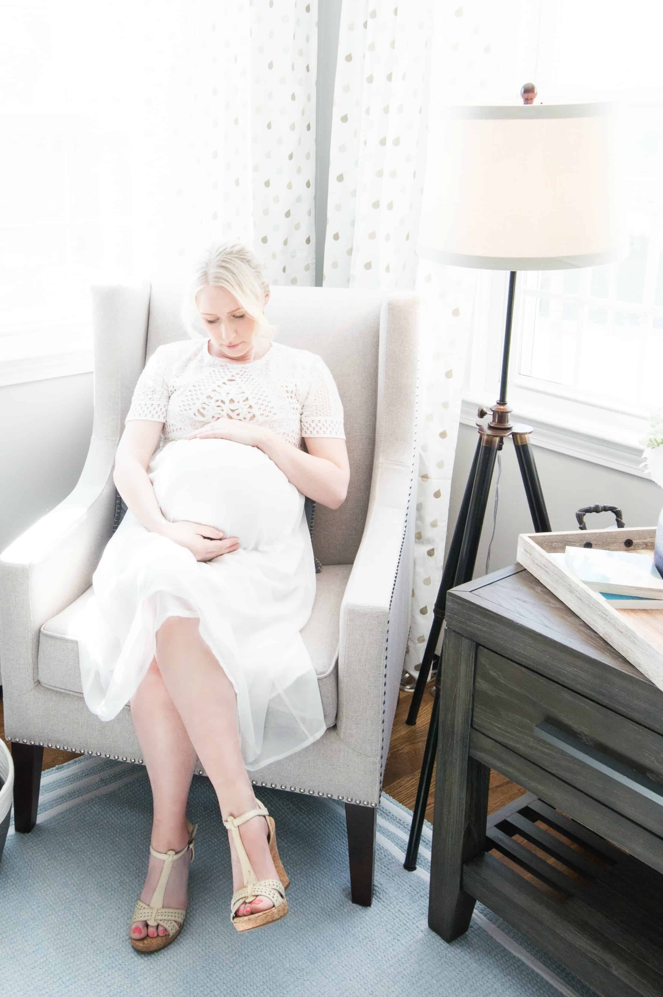 Pregnant mother to be sitting on white chair in classic and rustic blue and gray nursery