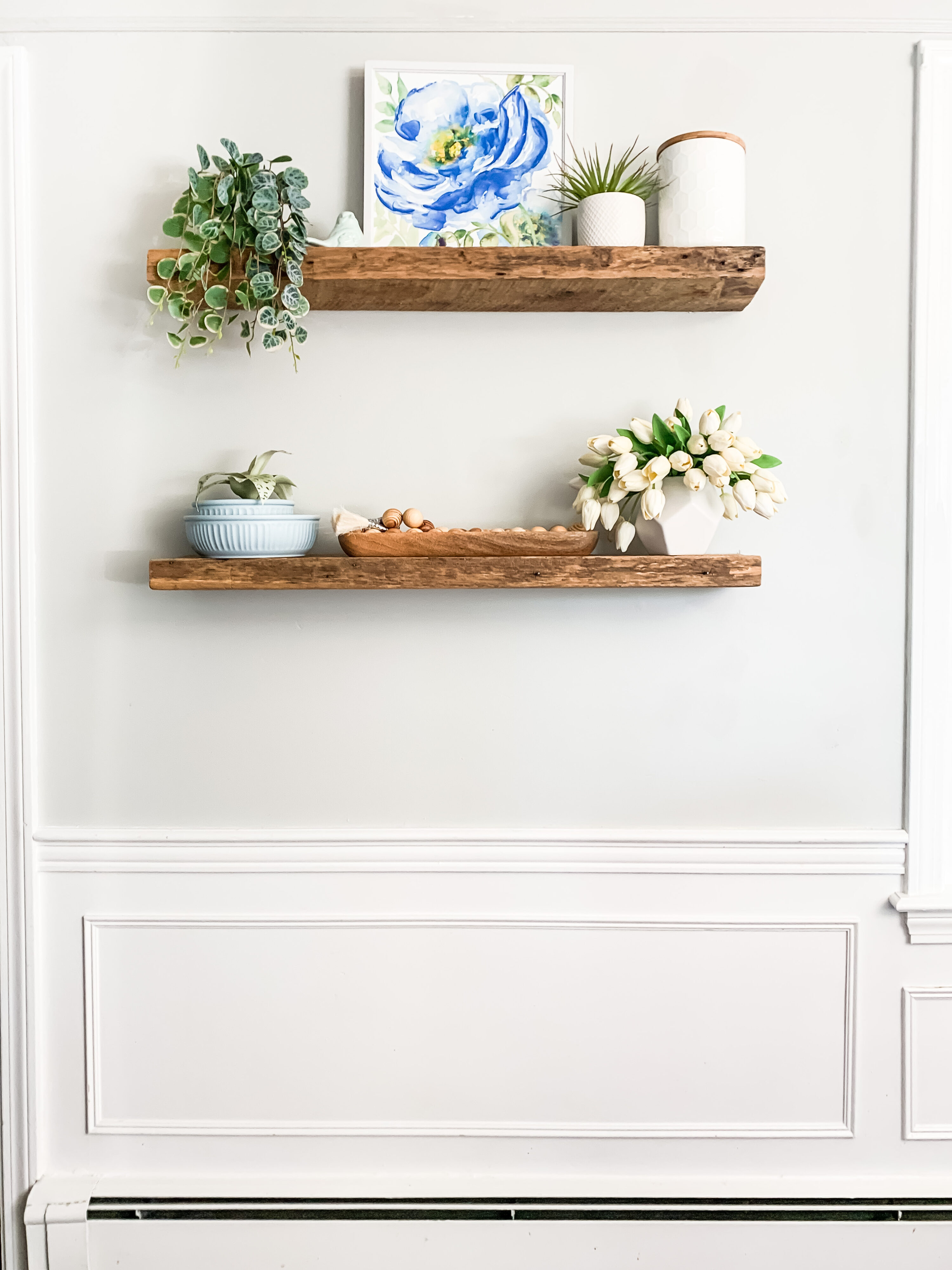 2 rustic floating wooden shelves, holding various pots of plants and swirly blue canvas art