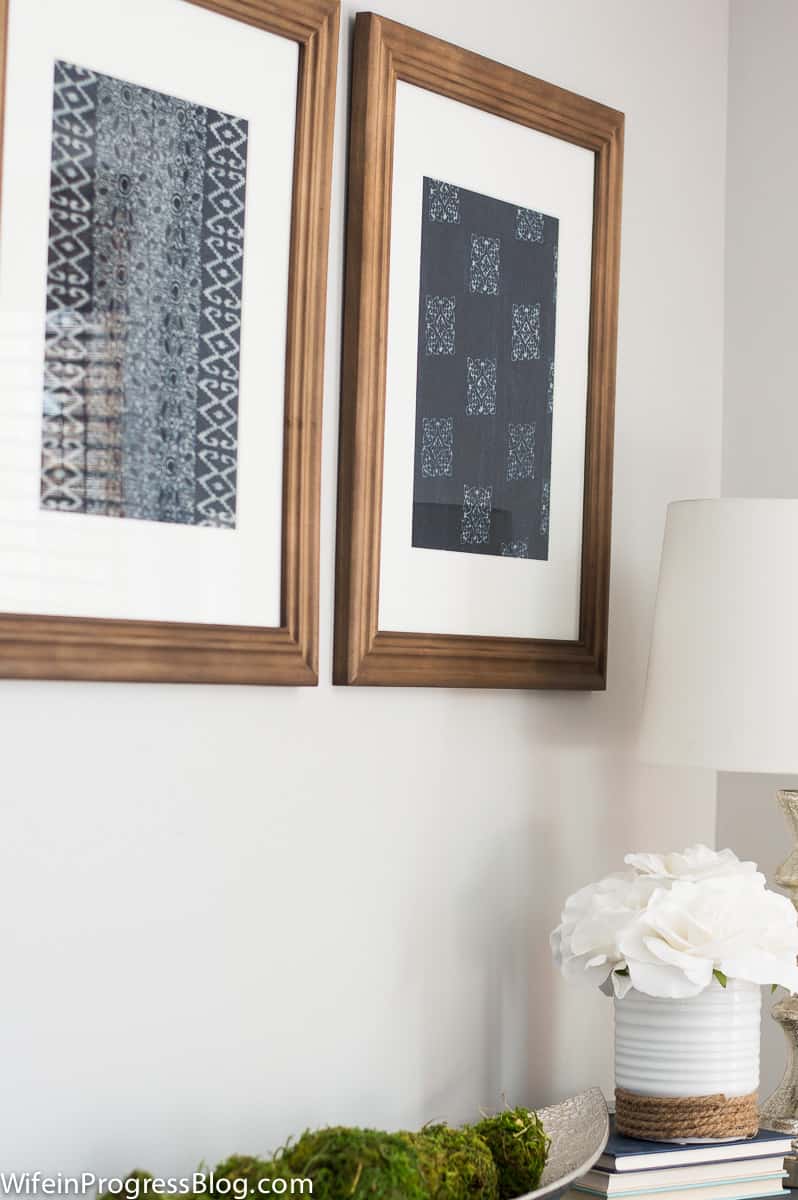 Another angle of the framed textile art, near a silver tray of green moss and a white ceramic vase with white silk flowers