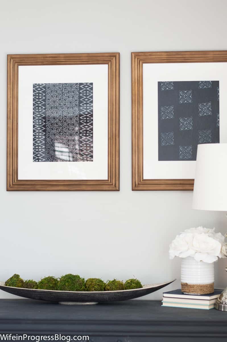 A pair of DIY textile art inspired by Pottery Barn,  in medium brown frames, above a table containing various decor items