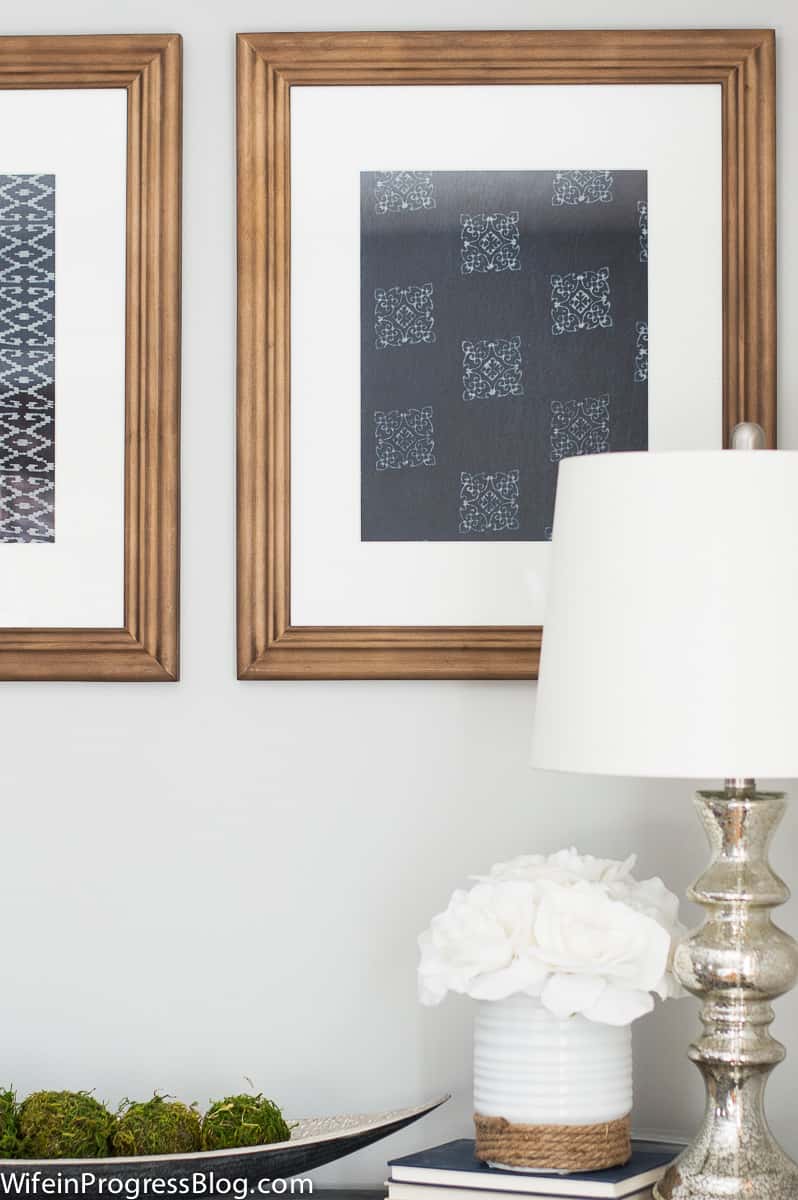 A close-up of one of the framed textile art pieces, showing intricate square white designs on a solid dark blue background