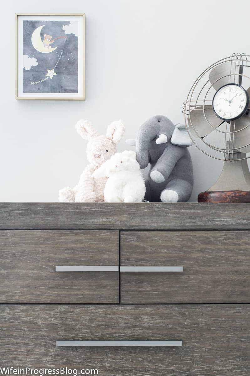 Baby nursery with clock and stuffed elephant set upon wooden dresser, and 