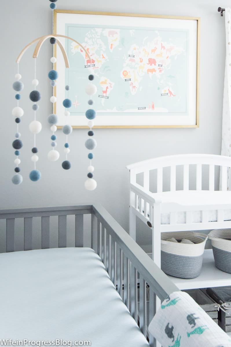 Blue and white mobile hanging above grey crib, and adorable world map with animals print on wall in baby nursery