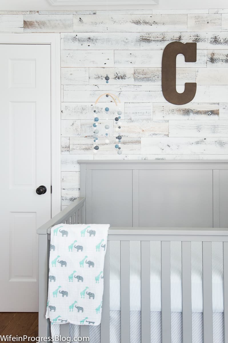 Grey crib and blue mobile set against reclaimed wood accent wall in baby boy nursery