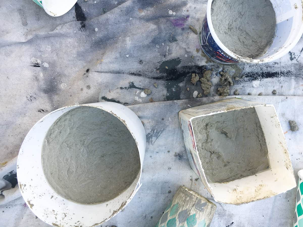 A group of three containers holding the first pour of concrete mix (2 round and 1 square), all resting on a drop cloth.