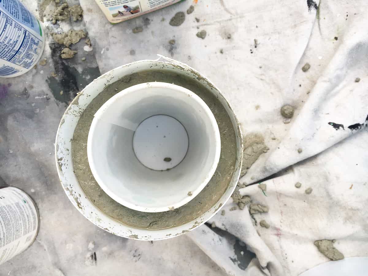 The top of a large plastic bowl with a ring of concrete, then a smaller plastic bowl in the middle, to form the shape of a concrete plant pot