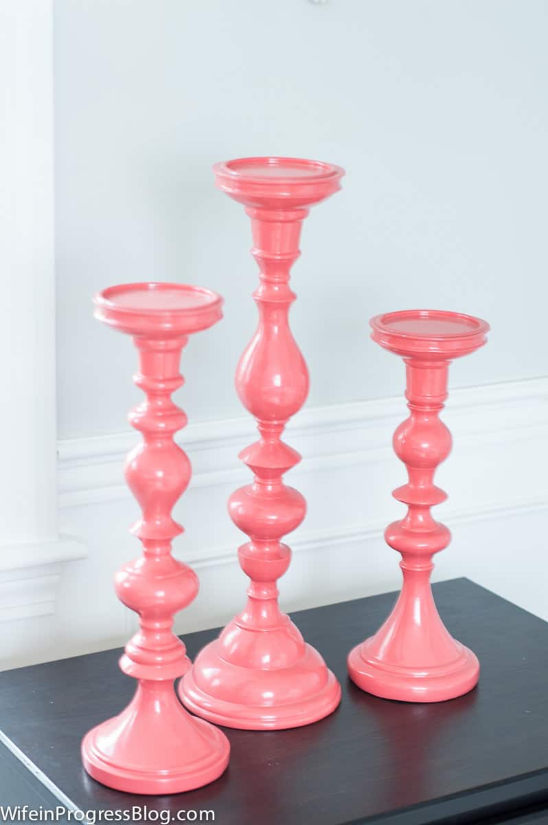 3 tall candlesticks in a bright coral color, resting on dark brown nightstand
