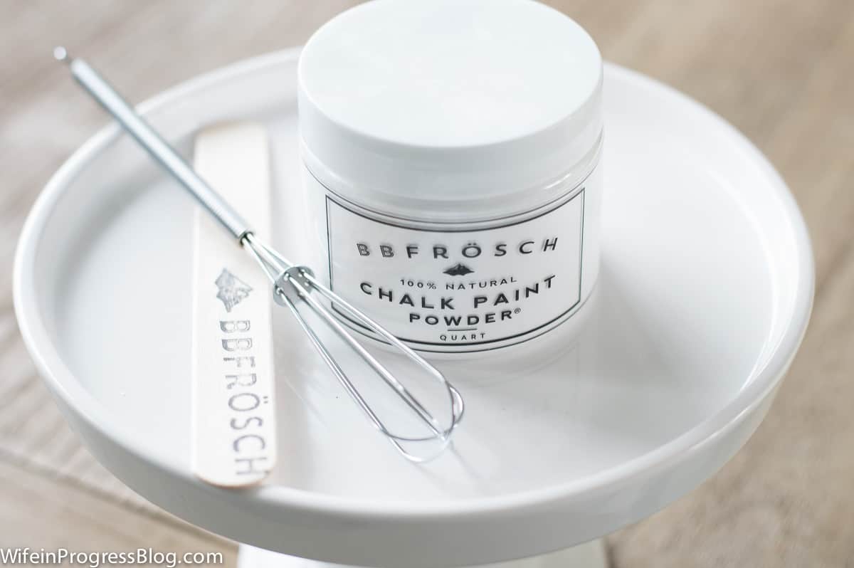 A quart container of BBFrosch chalk paint powder sitting in a plate with a whisk and wooden mixing stick