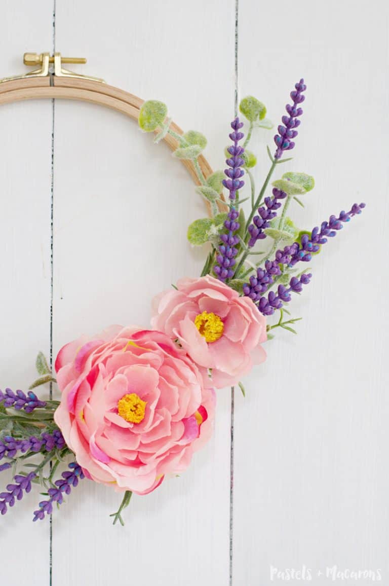 Bright pink flowers and a few sprigs of smaller, purple flowers and greenery on an embroidery hoop