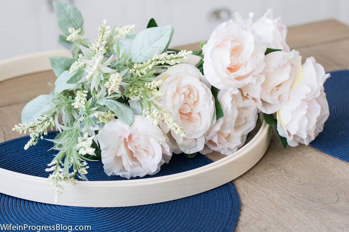 Light pink flowers and greenery on top of an embroidery ring, resting on round, blue place mats