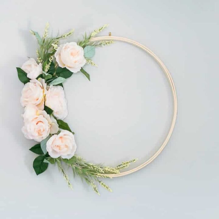 Wreath with an embroidery hoop base, covered on left side with light pink flowers and green sprigs