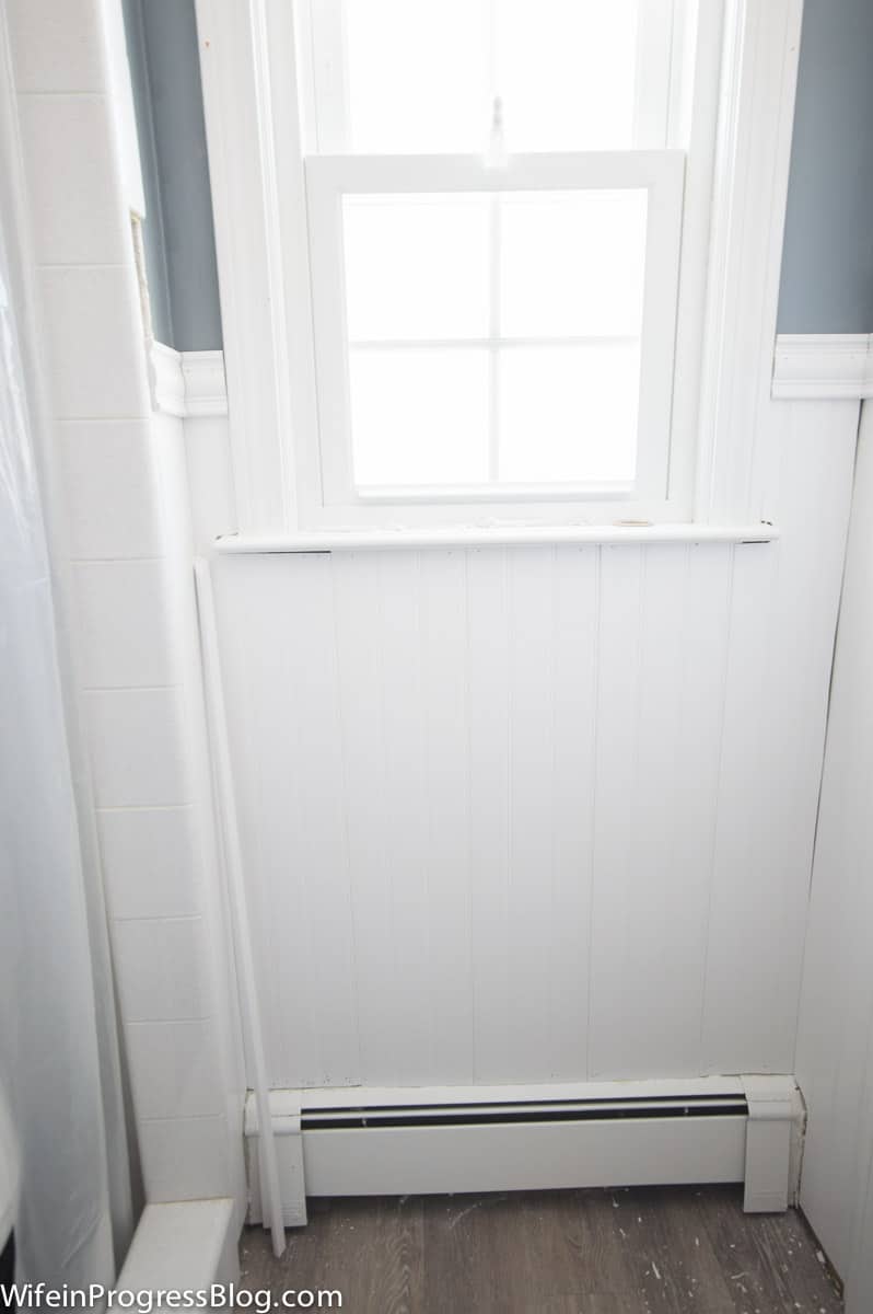 Bright window above vinyl wainscoting, with shower on left