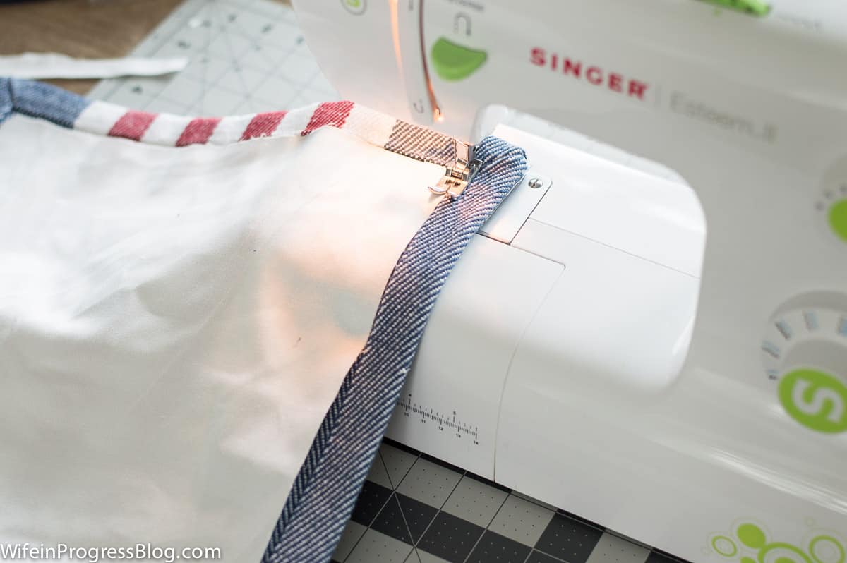 Using sewing machine to sew white fabric along the edge of patriotic placemat