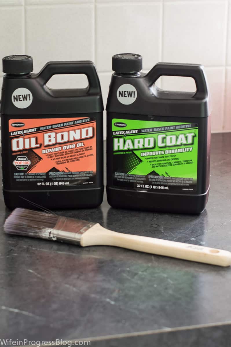 2 bottles of Crown brand \"Oil Bond\" and \"Hard Coat\" liquid products with a paint brush nearby on a counter top