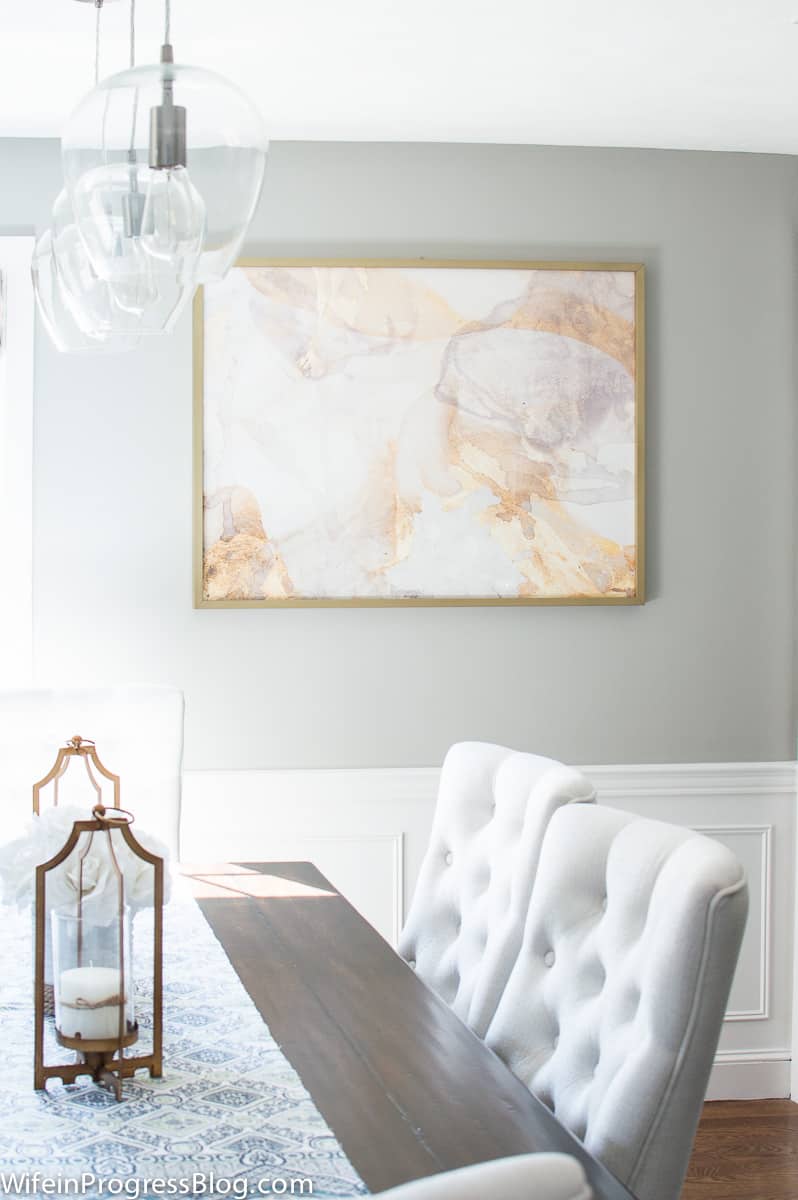 Dining room walls painted gray with large art hanging. Wainscoting is painted Benjamin Moore decorators white