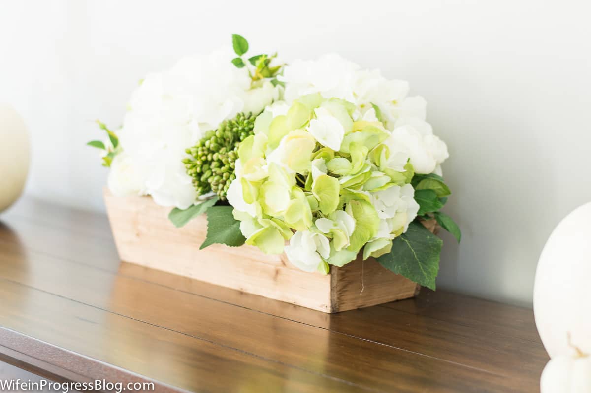 A rectangular, wooden box holding large, green and white flowers on top of a wooden table