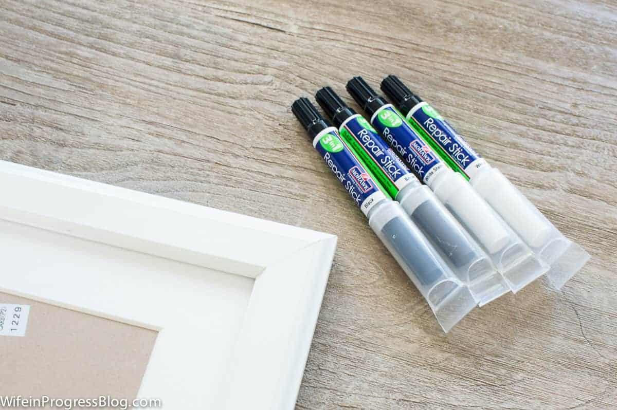 Four paint repair sticks specially designed for IKEA furniture, resting on a table, next to a white photo frame