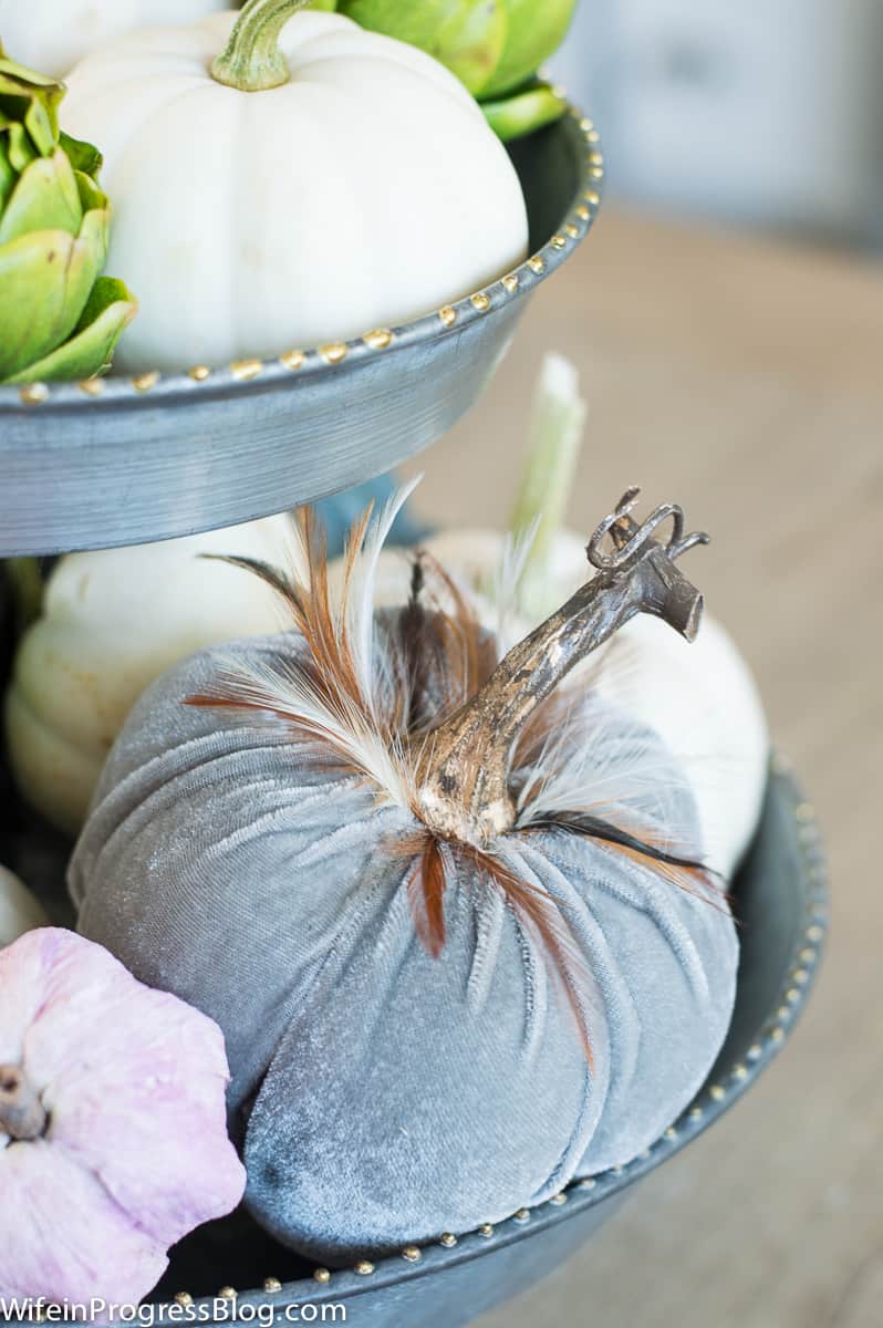A grey fabric pumpkin in the bottom of a tiered metal tray