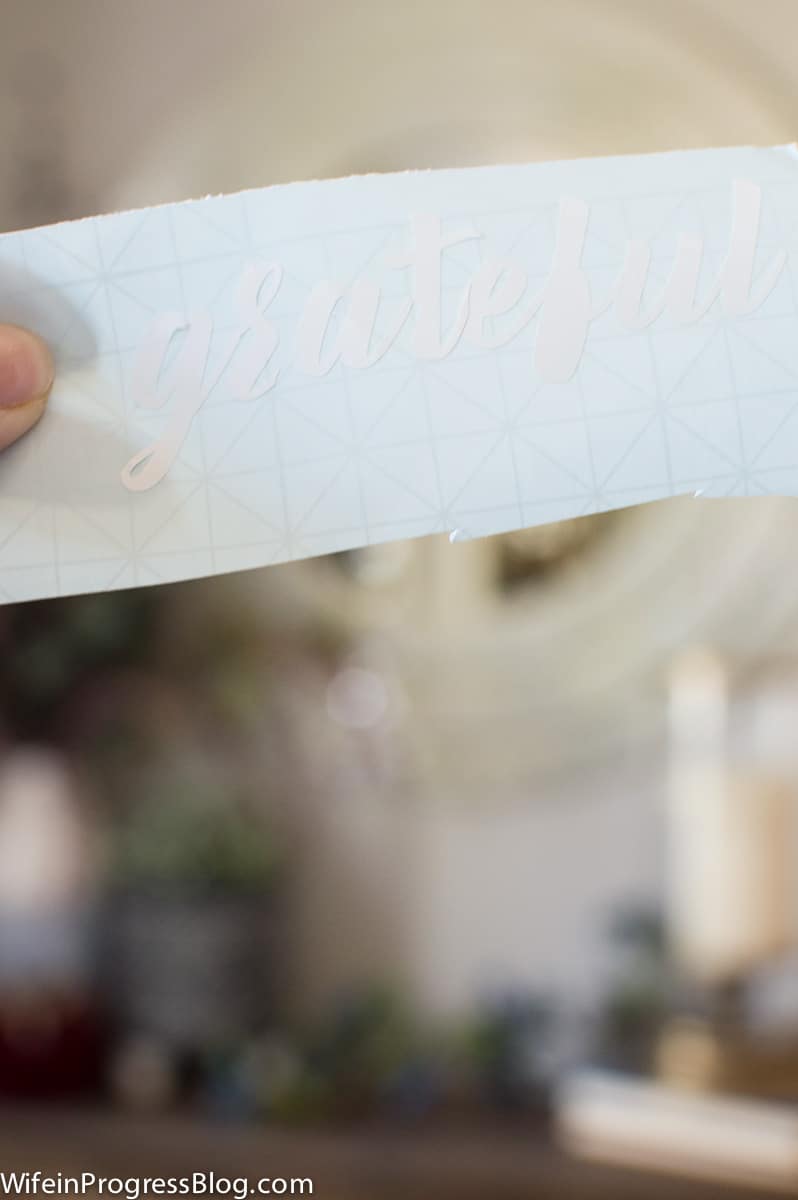 The word \"grateful\" on a vinyl sticker, still attached to the sticker paper