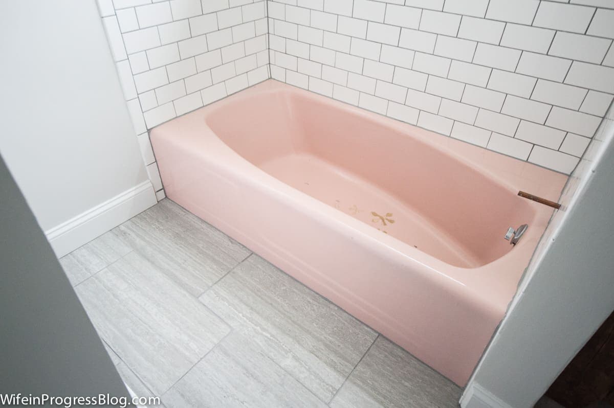 A pink tub, white subway tile around tub walls, and large, rectangular grey tiles on floor