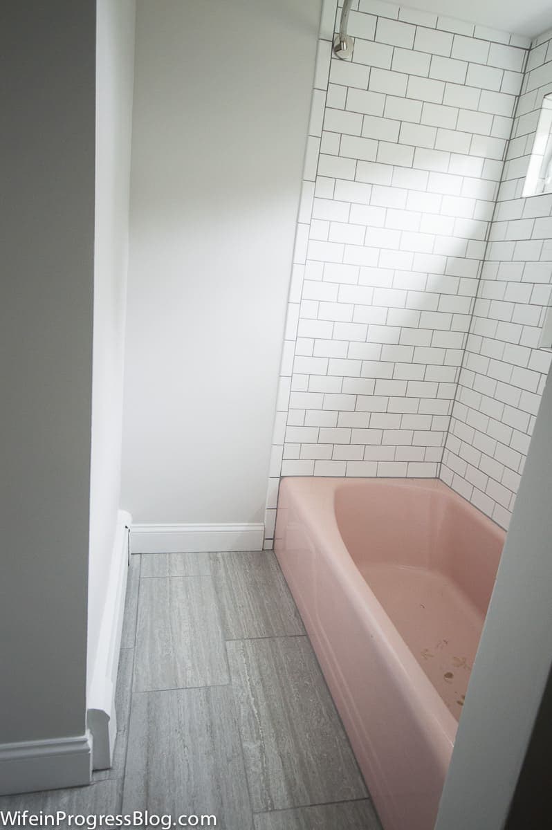 A pink tub, white subway tile around tub walls, an oblong window above and a curtain rod