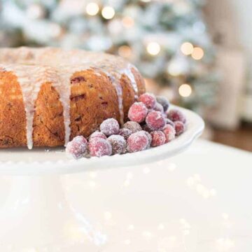 closeup of cranberry cake with sugared cranberries on the side with Christmas tree in the background