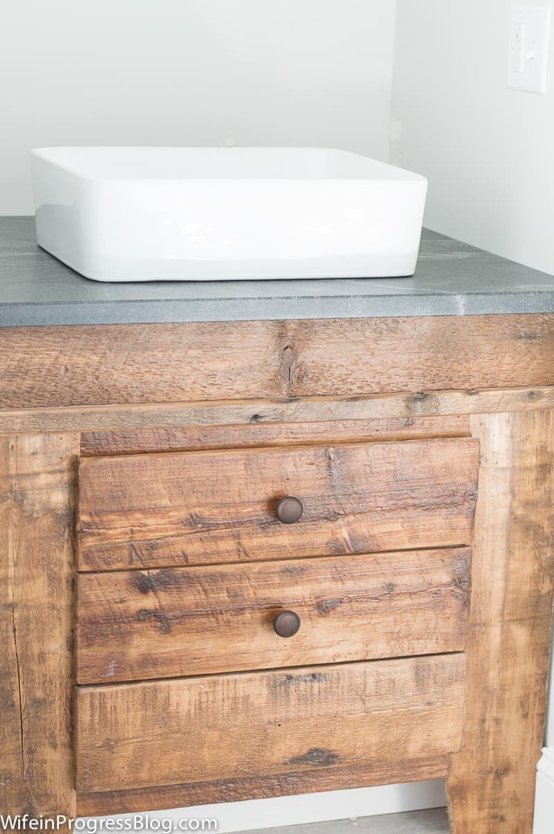 A rectangular, white vessel sink on top of a wooden cabinet