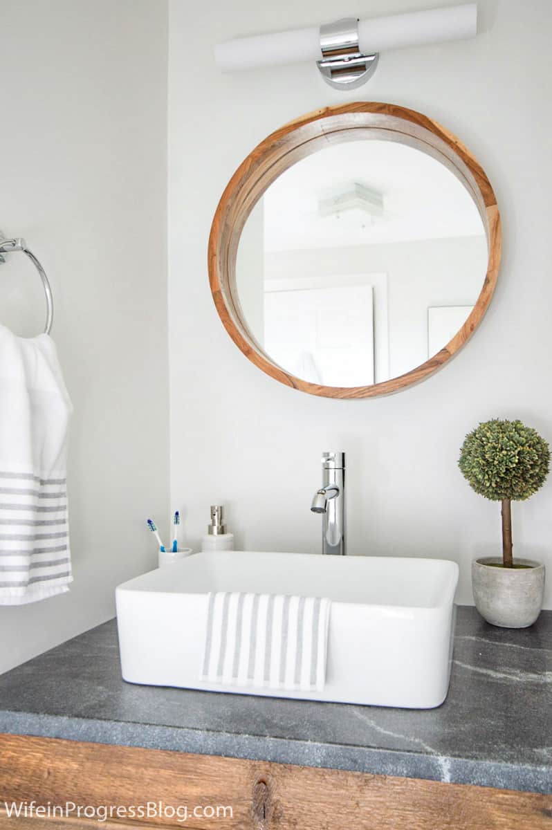 Large round wood-framed mirror complements straight lines of light fixture, vessel sink and wood vanity